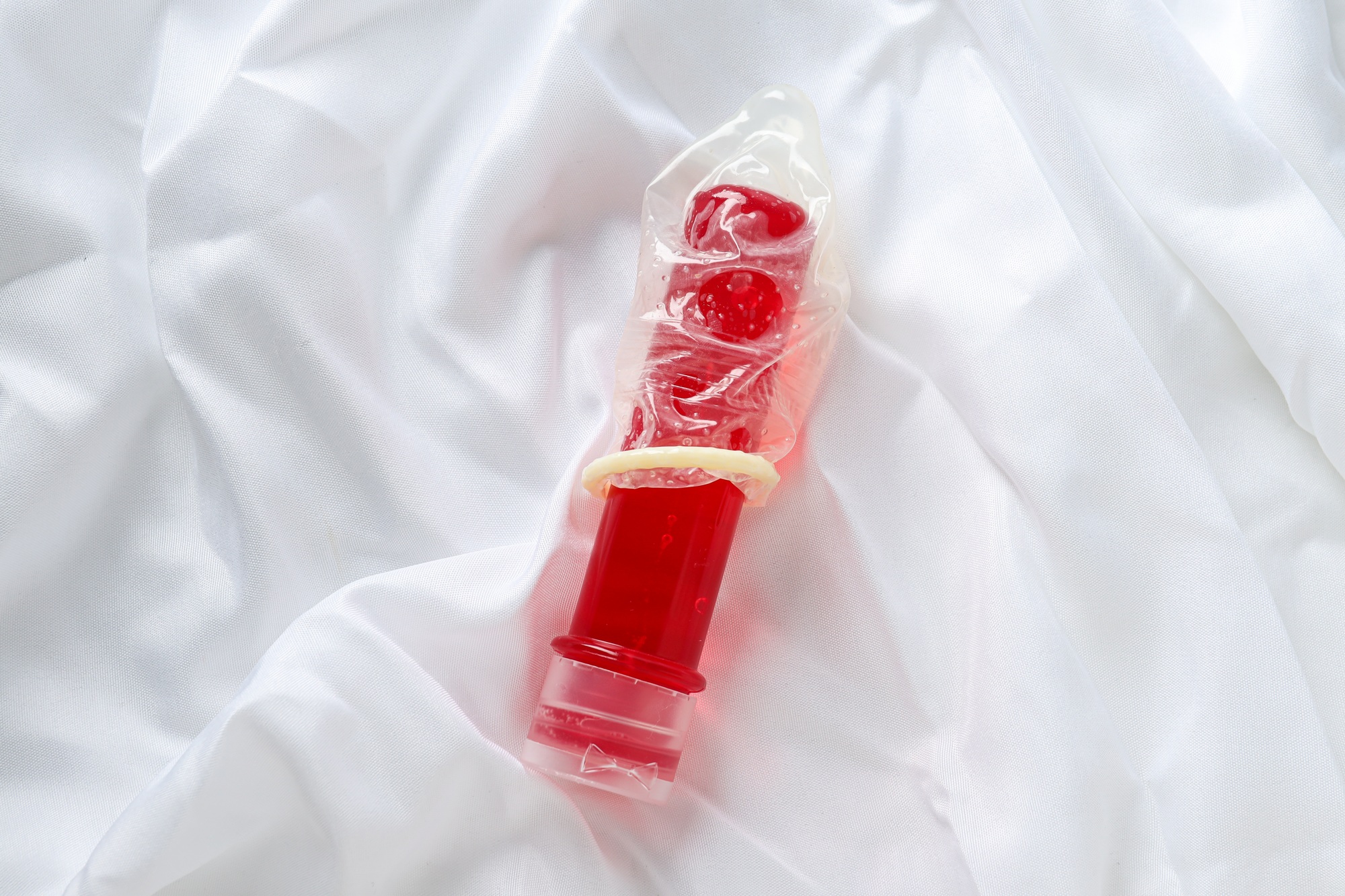 Condom on a red bottle with lubricant on a white background