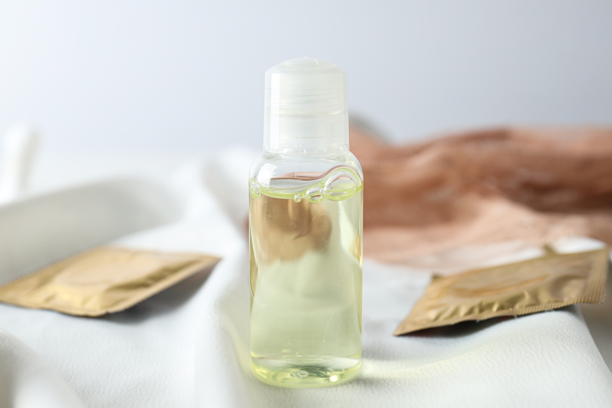 Lubricant in a transparent bottle with condoms on a light background