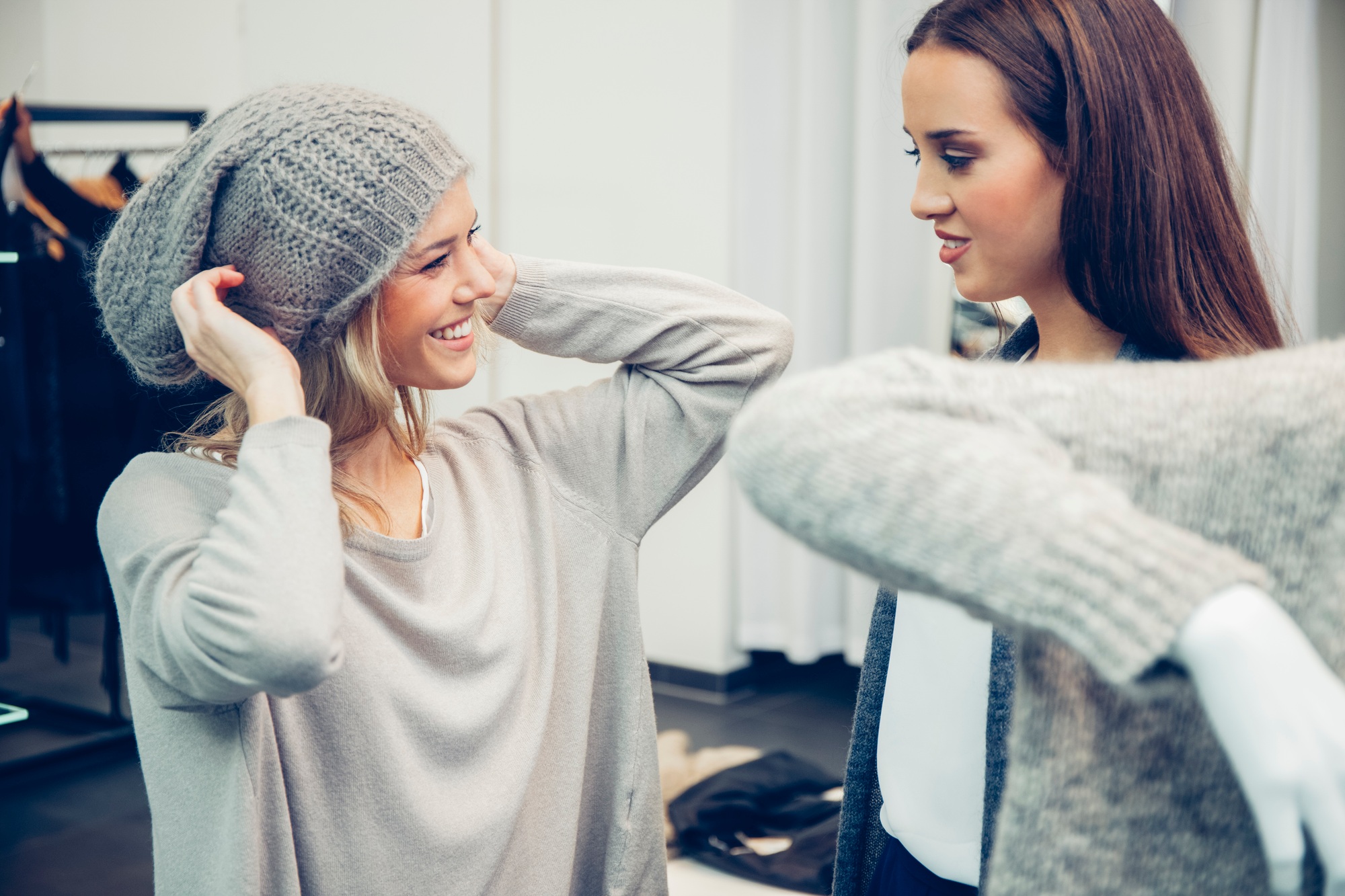 Young woman assisted by friend putting on woolly hat in a boutique